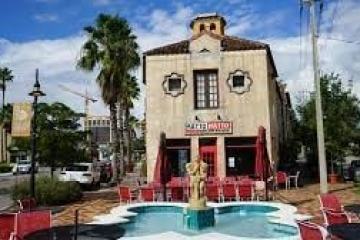 Cafe patio with fountain in front of a Mediterranean-style building under a blue sky.