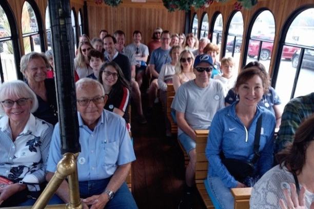 Group of people smiling and sitting in a wooden trolley with arched windows.