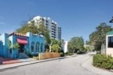 Colorful buildings and trees line an empty street under a clear blue sky.