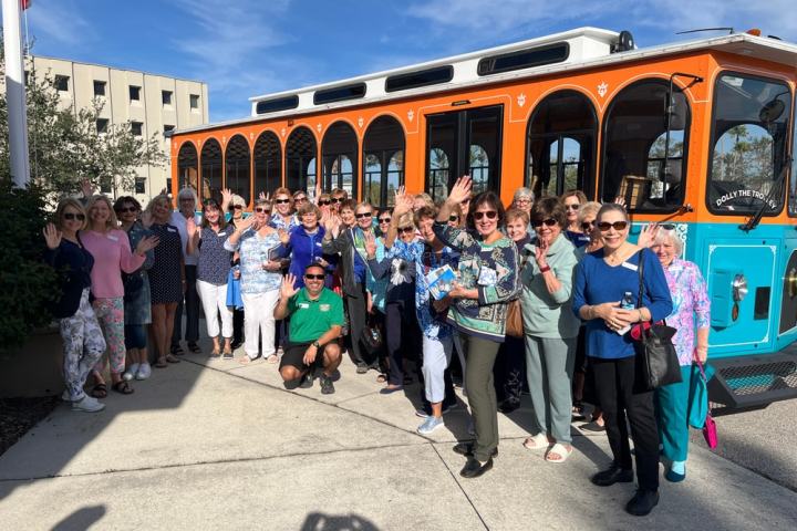 Group of people waving in front of an orange and turquoise trolley.