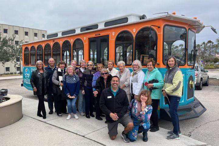 Group of people posing in front of an orange and blue trolley on a cloudy day.