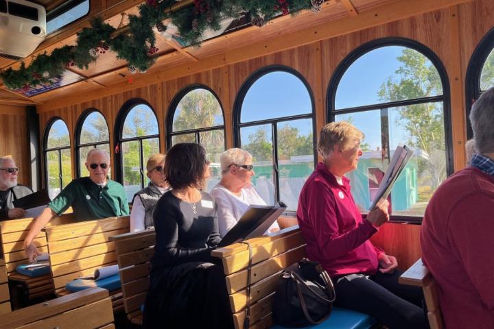 People on a decorated trolley reading papers with sunlit windows in the background.