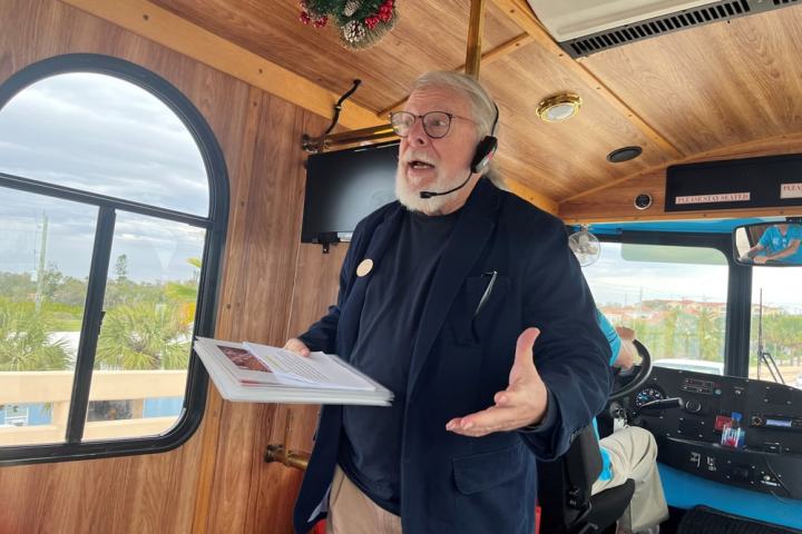 Man with headset and papers speaking on a bus with wood interior.
