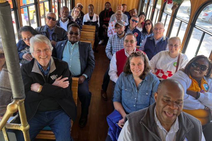 A group of people seated inside a wooden trolley, smiling towards the camera.