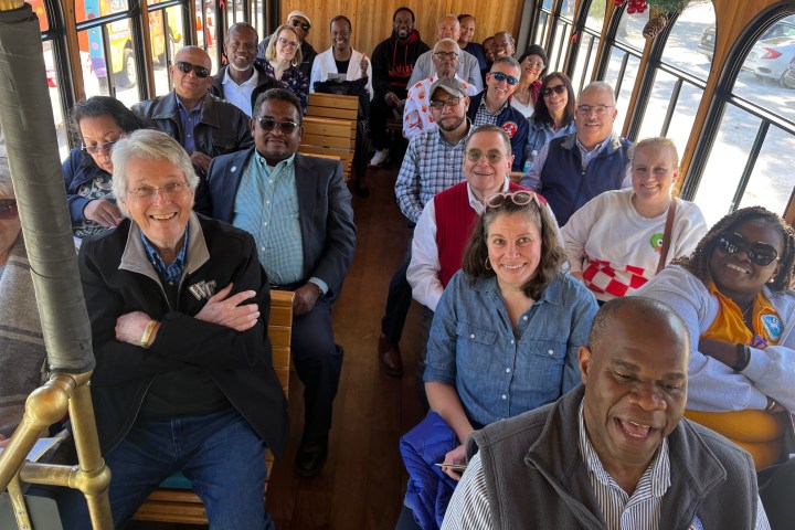 Group of people sitting inside a wooden trolley, smiling and facing the camera.