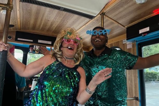 Two people in sparkly outfits and fun glasses dancing on a bus.