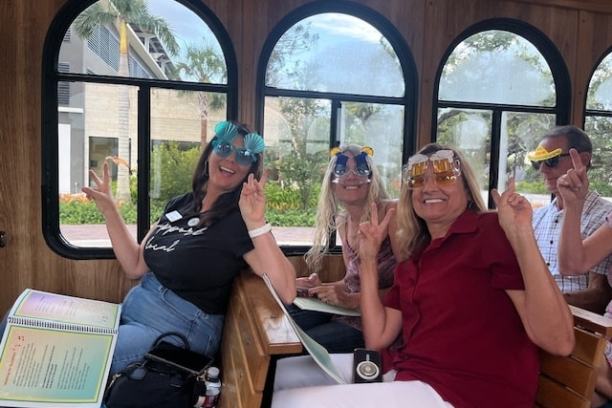 Three women on a bus wearing novelty glasses, posing with peace signs.