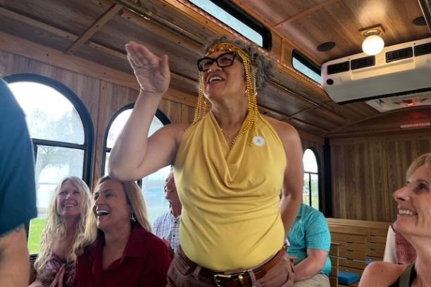 Person in yellow waves inside a trolley with smiling passengers.