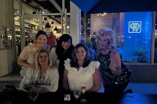 Five women posing together at an outdoor restaurant table at night.