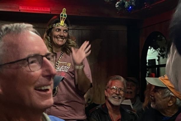 Group of smiling people indoors, one woman wearing a birthday crown.