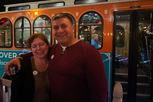 Smiling couple standing in front of an orange and blue trolley at night.
