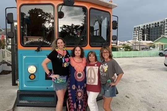 Four women posing in front of a colorful trolley on a cloudy day.