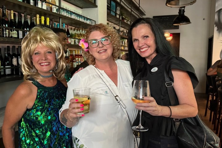 Three women smiling and holding drinks in a bar.