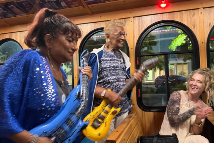 Three people play toy guitars and clap on a wooden bus.