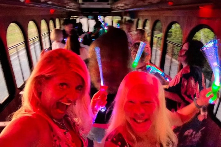People on a party bus, holding glowing light sticks with colorful lighting.