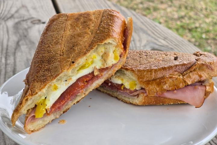 Toasted sandwich with meat and cheese on a white plate on a wooden table.
