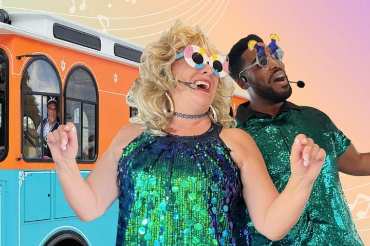 Two people in glittery outfits with fun sunglasses dancing in front of a colorful trolley.