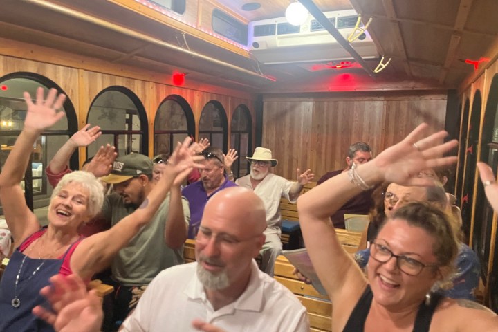 a group of people sitting on the sing-along trolley and waving their arms