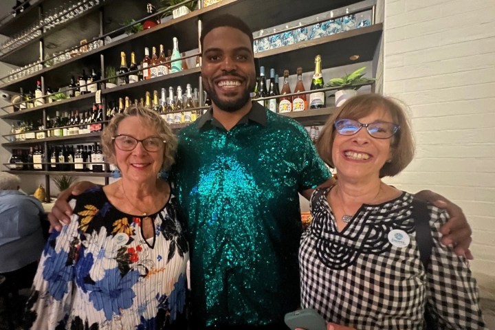 Three people smiling in a bar with bottles in the background.