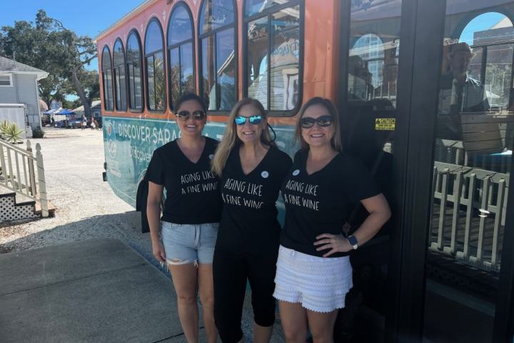 Three women in matching shirts pose beside a trolley.