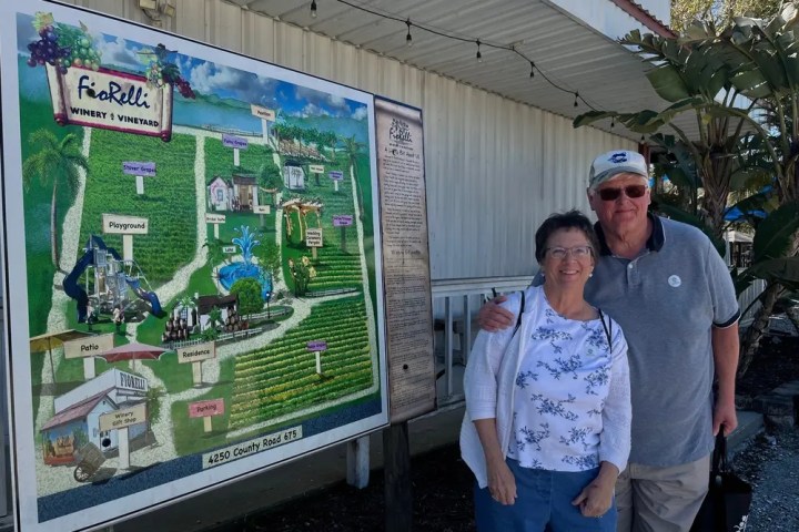 Two people stand smiling in front of a winery map display outdoors.