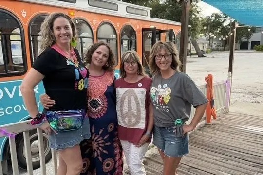 Four women smiling in front of an orange trolley.