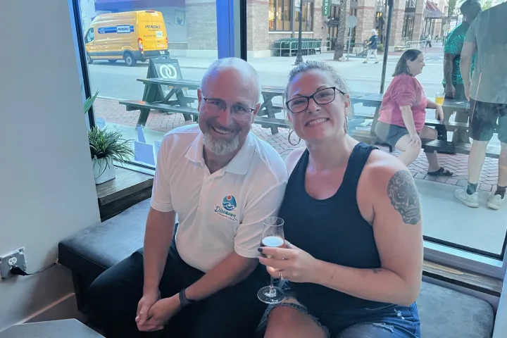 a man and woman sitting next to a glass of wine outside of 99 bottles on the sing-along trolley
