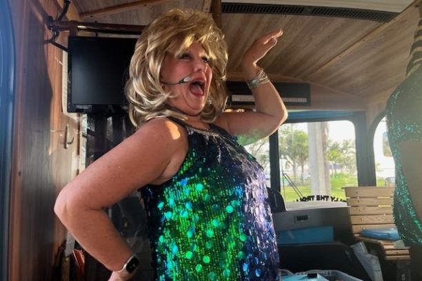 Person in sequined dress and headset performing inside a bus with a lively expression.