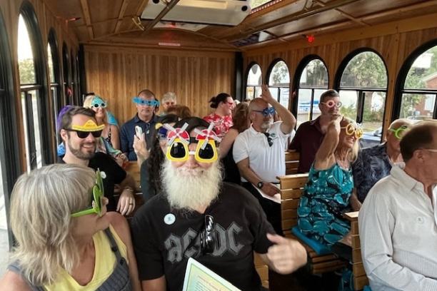 Group of people on a trolley wearing colorful, playful sunglasses.
