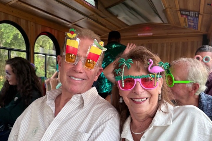 Two people on a bus wearing novelty tropical sunglasses, smiling.