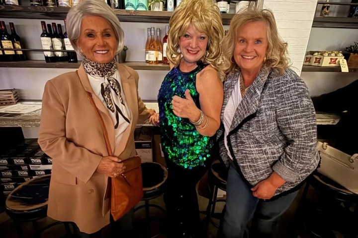 Three smiling people in a bar, one in a green sequin dress, standing together.