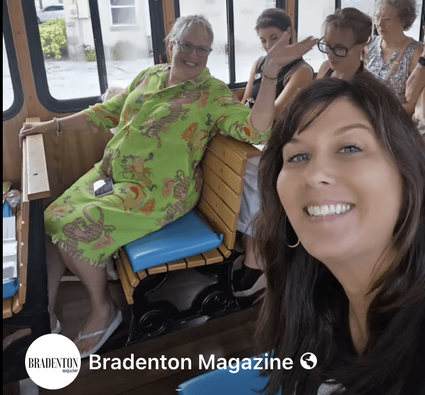 Kelly and Tammy on Sing Along – Bradenton Magazine Group of smiling people sitting inside a wooden trolley with blue seats.