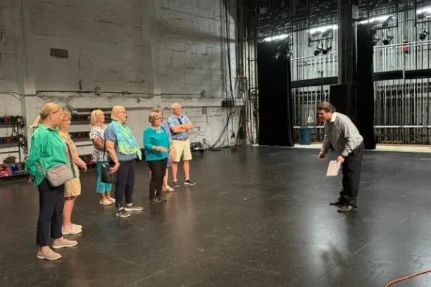 Group of people listening to a guide on an empty theater stage.