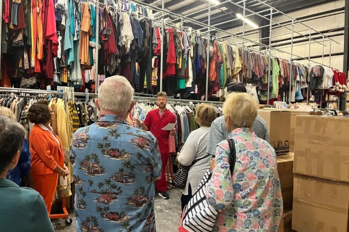 Group touring a large clothing warehouse with racks of colorful garments.