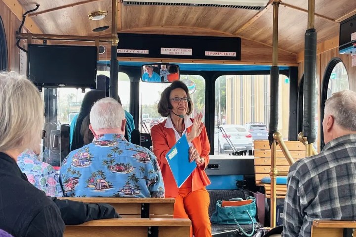 Woman in orange suit talking to people on a bus tour.