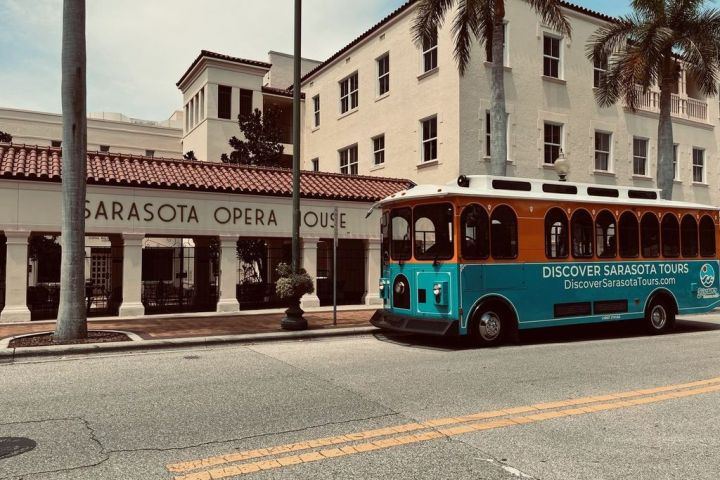 Sarasota Opera House with a tour trolley parked in front, palm trees lining the street.