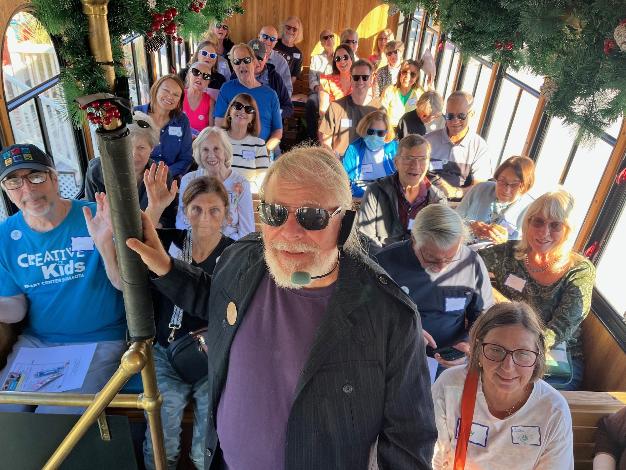 Group of people smiling inside a decorated tram car, with a man in front wearing a headset.