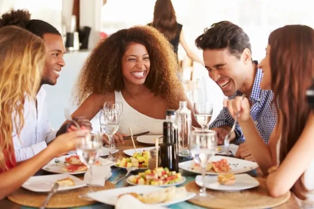 Group of people laughing while dining together at a table.