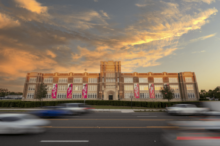 Historic building with banners at sunset, cars passing on road.