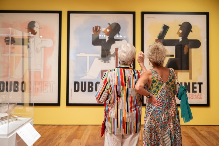 Two people observe Dubonnet posters in an art gallery.