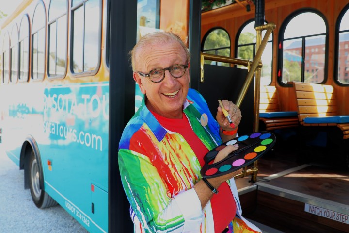 Smiling man with paint palette standing by a colorful trolley bus.