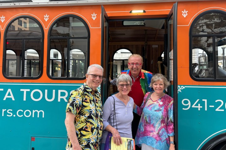 Four adults in colorful shirts standing by an orange tour bus.