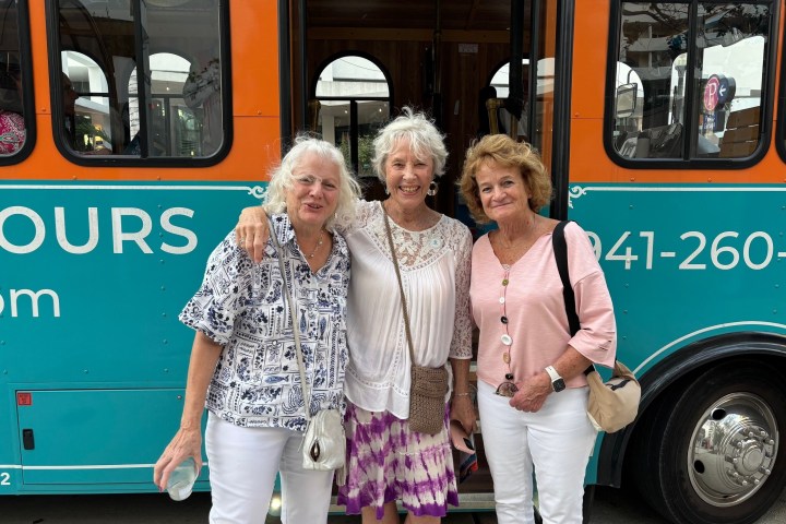Three women smiling and standing in front of a trolley bus.