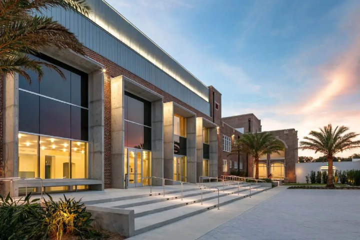 Modern building with tall windows, palm trees, and a sunset sky.