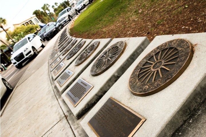 Bronze plaques on sidewalk, depicting various designs, with cars parked on the street in the background.