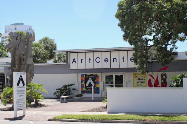Exterior view of a modern art center with colorful banners and a large tree.