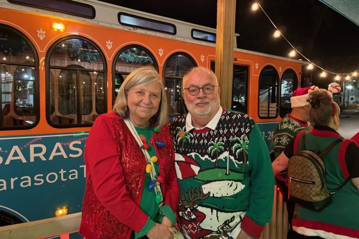 Two people in festive attire posing in front of an orange trolley.