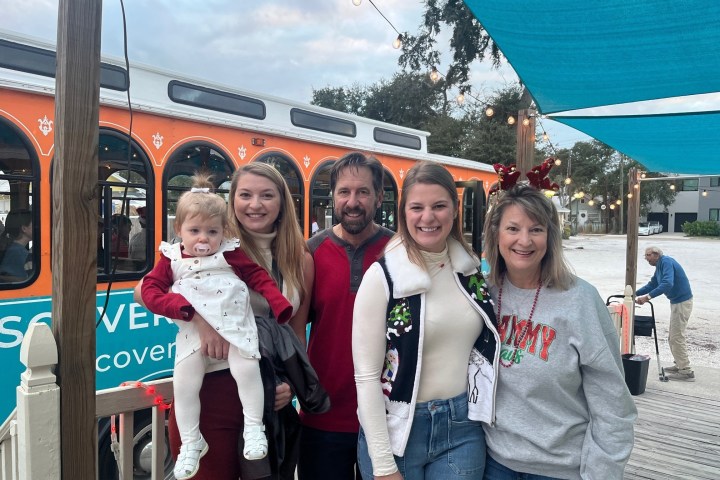 Family group posing in front of an orange trolley, under a blue canopy, with holiday attire.