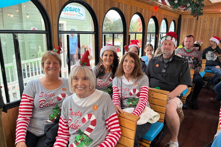 Group of people in festive clothing on a wooden tram decorated with Christmas garlands.