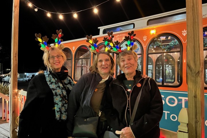 Three women with reindeer headbands in front of a decorated tram car.